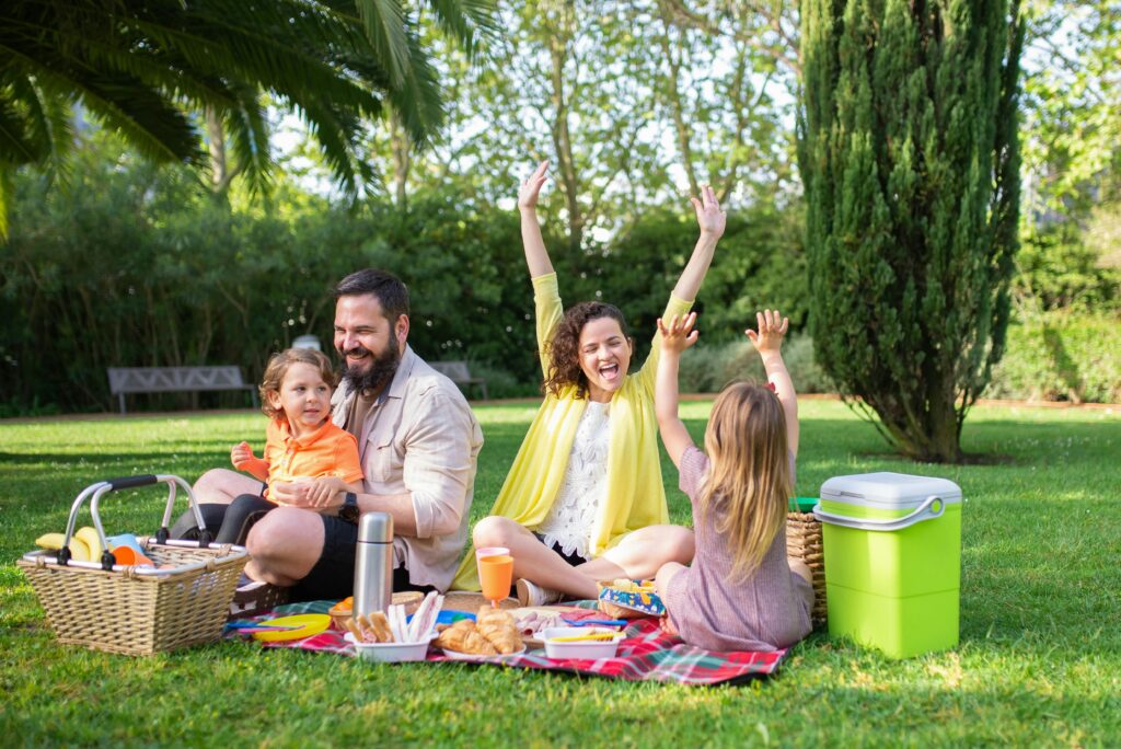 Happy family enjoying a sunny picnic with children on a blanket in a Portugal park.